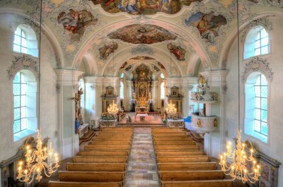 Pfarrkirche "Zum Heiligen Wolfgang" Eine wunderschöne Kircheninneneinrichtung mit gewölbter Decke und kunstvollen Fresken. Das Interieur ist hell erleuchtet und zeigt Holzbänke sowie goldene Kronleuchter.