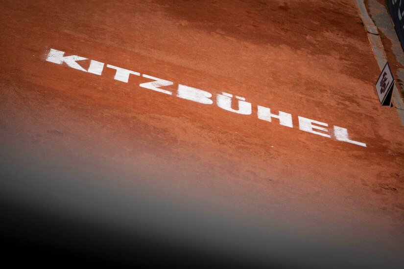 Weißer Kitzbühel-Schriftzug auf einem roten Sandtennisplatz.