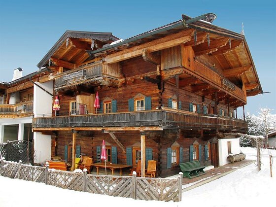 Mehrstöckiges Holzhaus im Alpenstil mit Balkonen in einer verschneiten Winterlandschaft.
