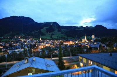 Abendlicher Blick vom Café Kitzblick Blick von einer Terrasse auf die beleuchtete Stadt Kitzbühel bei Dämmerung vor bewaldeten Bergen.