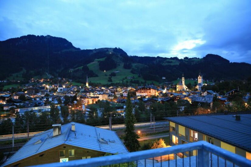 Abendlicher Blick vom Café Kitzblick Blick von einer Terrasse auf die beleuchtete Stadt Kitzbühel bei Dämmerung vor bewaldeten Bergen.