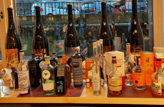 Auswahl regionaler Spirituosen Verschiedene Spirituosenflaschen wie Gin, Rum und Wein stehen auf einer Holztheke vor einem Fenster.