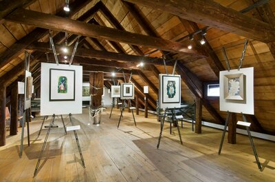 Museum Ein Ausstellungsraum mit mehreren Kunstwerken auf Ständern. Die Holzdecke und der Boden verleihen dem Raum eine gemütliche Atmosphäre.