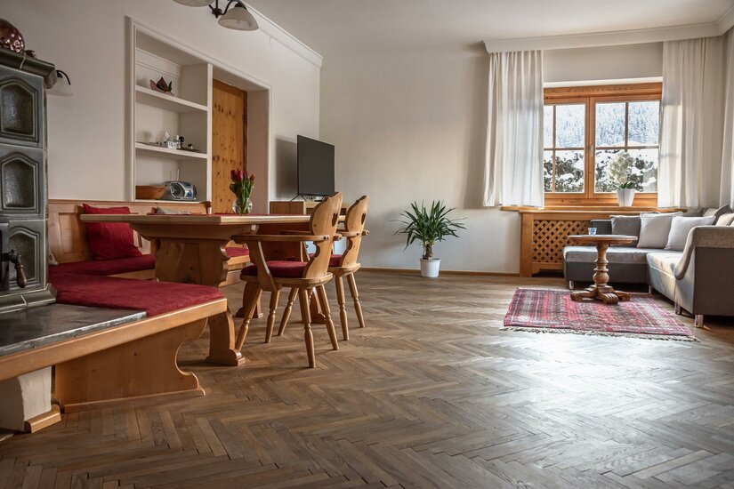 Wohnzimmer mit Holzesstisch, Eckbank, Kachelofen und Sofa auf Parkettboden.