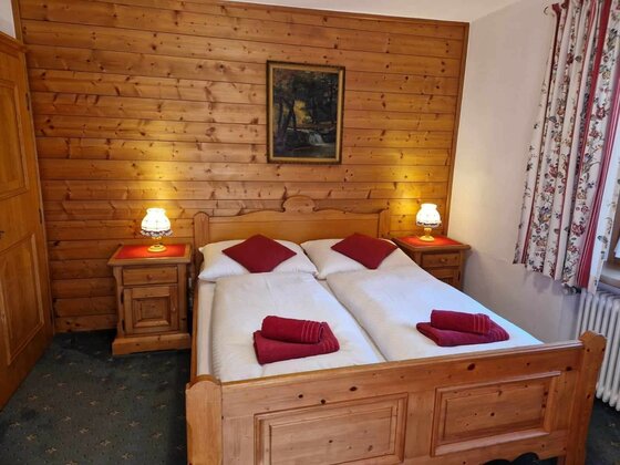 Doppelbett aus Holz vor einer holzgetäfelten Wand mit zwei Nachttischen und Lampen.