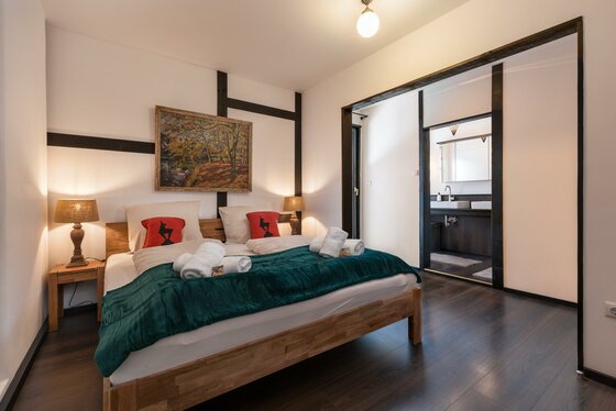 Schlafzimmer 1 Hornbichl Modernes Doppelzimmer mit Holzrahmenbett, dunklem Boden und Blick in das angrenzende Badezimmer.