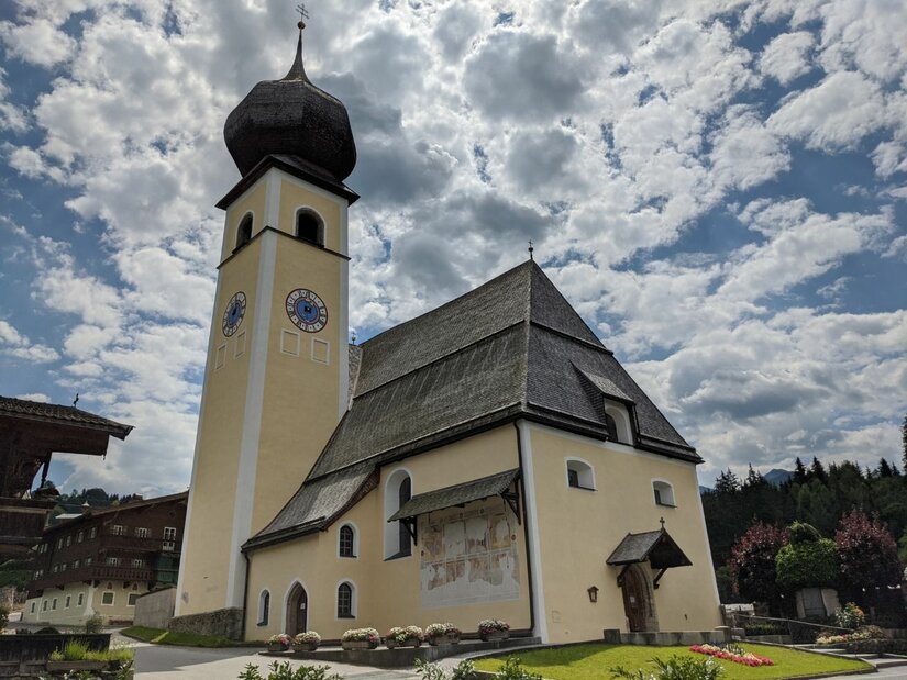 Pfarrkirche Aurach bei Kitzbühel Pfarrkirche in Aurach mit markantem Zwiebelturm und Schindeldach vor bewölktem Himmel.