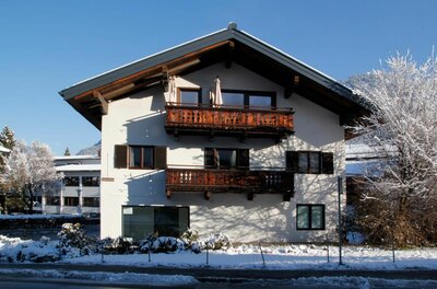 Alpines Wohnhaus mit Holzbalkonen im Schnee unter blauem Himmel.