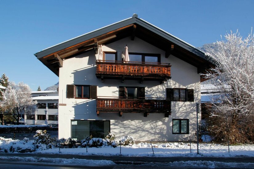 Winteransicht Appartement Elisabeth Alpines Wohnhaus mit Holzbalkonen im Schnee unter blauem Himmel.