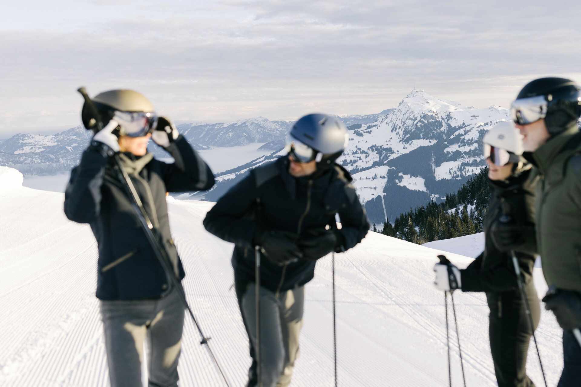 Eine Gruppe von Skifahrern steht auf einer schneebedeckten Piste im Skigebiet Kitzbühel und bereitet sich auf die Abfahrt vor, umgeben von Bergen.