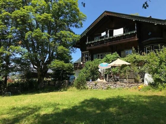 Dunkles Holzhaus mit Balkon, Terrasse und Garten unter blauem Himmel.