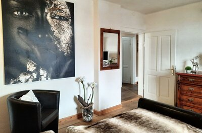 Schlafzimmer im Haus Brugger Schlafzimmer mit großem Porträtgemälde, Ledersessel, Holzboden und einer Kommode.