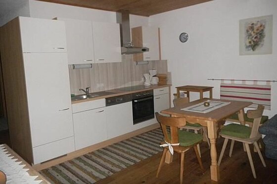 Küche im Seiwaldhof Brandstätter Moderne Küchenzeile mit weißen Fronten und angrenzendem Holzesstisch mit Stühlen.