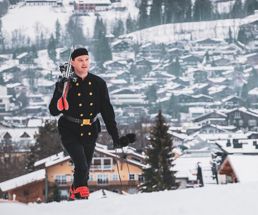 A chimney sweep walking up a slope with his tools and a pair of skiis