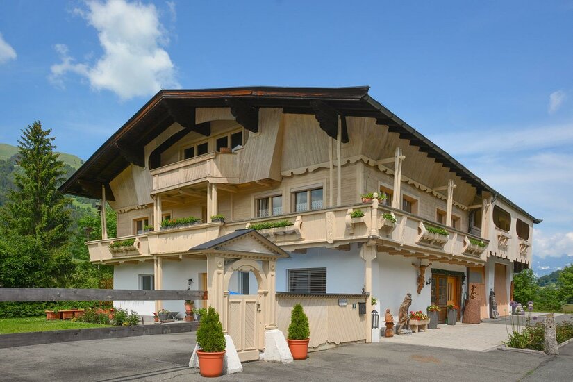 Zweistöckiges Gebäude in Holzbauweise mit Balkonen, Blumenkästen und einem kleinen Holztor im Vordergrund.