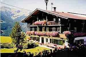 Alpines Haus im Sommer Mehrstöckiges Holzhaus mit blumengeschmückten Balkonen vor einer Bergkulisse.