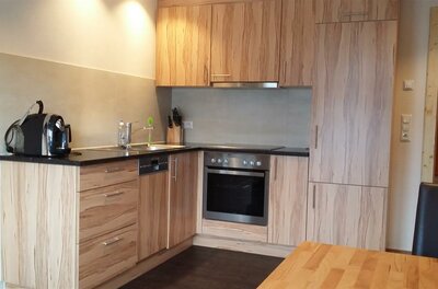 Moderne Einbauküche in L-Form mit hellen Holzfronten, Backofen, Ceranfeld und Kaffeemaschine.