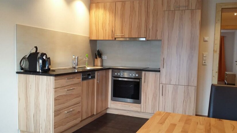 Küche der Wohnung EG1 Moderne Einbauküche in L-Form mit hellen Holzfronten, Backofen, Ceranfeld und Kaffeemaschine.