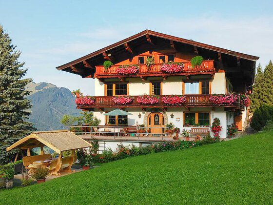 Hof Hamoos im Sommer Alpiner Bauernhof mit Blumenschmuck an den Holzbalkonen und einer Sitzgruppe im Garten.