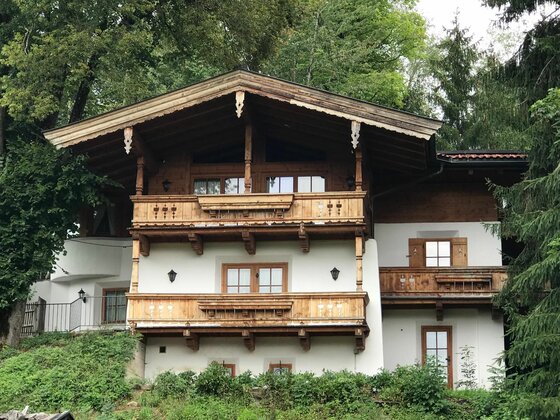 Das Kitz Reith im Sommer Mehrstöckiges Alpenhaus mit Holzfassade, Balkonen und weißem Putz vor Waldhintergrund.