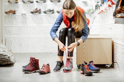 Schuhberatung bei Kitzsport Pepi Eine Frau sitzt in einem Sportgeschäft und schnürt einen grauen Wanderschuh mit pinken Akzenten.