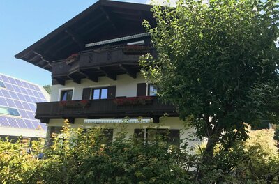 Haus Pankratz Mehrstöckiges Alpenhaus mit dunklen Holzbalkonen, Blumenkästen und Photovoltaikanlage im Hintergrund.