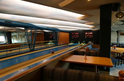 K&K Kegelbahn & Kulturhaus Innenansicht einer Kegelbahn mit blauen Bahnen, Holztischen und Sitzbänken.