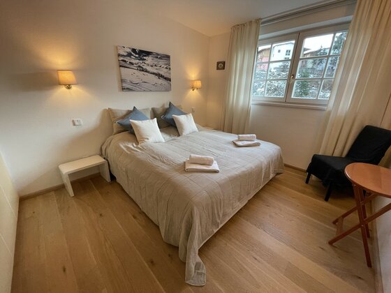 Schlafzimmer mit Doppelbett, Parkettboden, Wandleuchten und Fenster mit Blick auf Häuser.