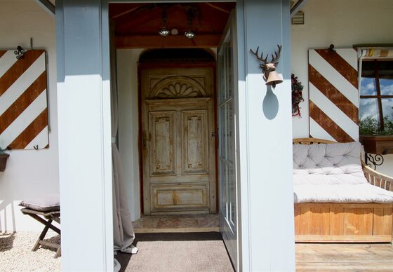Eingangsbereich Chalet Belle Kitz Eingangsbereich eines Chalets mit verzierter Holztür, rot-weiß gestreiften Fensterläden und einer Holzbank.