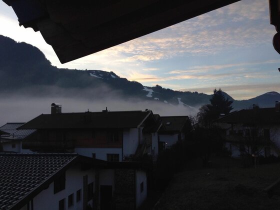 Aussicht vom Haus Haas Blick über Hausdächer auf nebelverhangene Berge bei Dämmerung.
