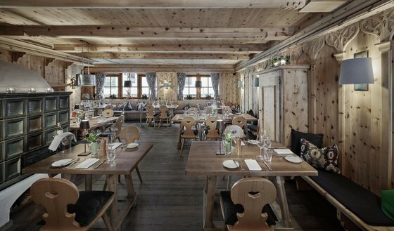 Neuwirt Zirbenstube Rustikale Gaststube mit Holztischen, Stühlen mit Herz-Ausschnitt, Kachelofen und holzgetäfelten Wänden.