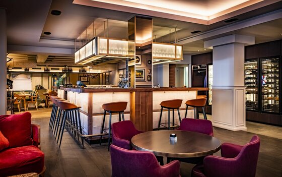 Neuwirt Bar Moderne Hotelbar mit beleuchteter Theke, Barhockern und Sesseln im Innenraum.