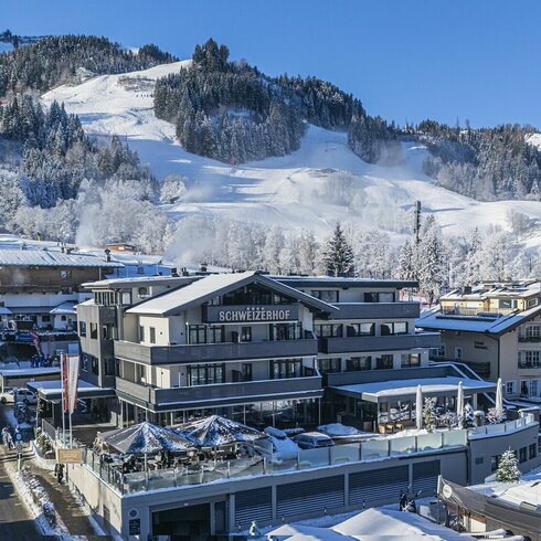 Ein malerisches Winterdorf mit schneebedeckten Bergen und einem modernen Hotel, das in der Sonne strahlt.