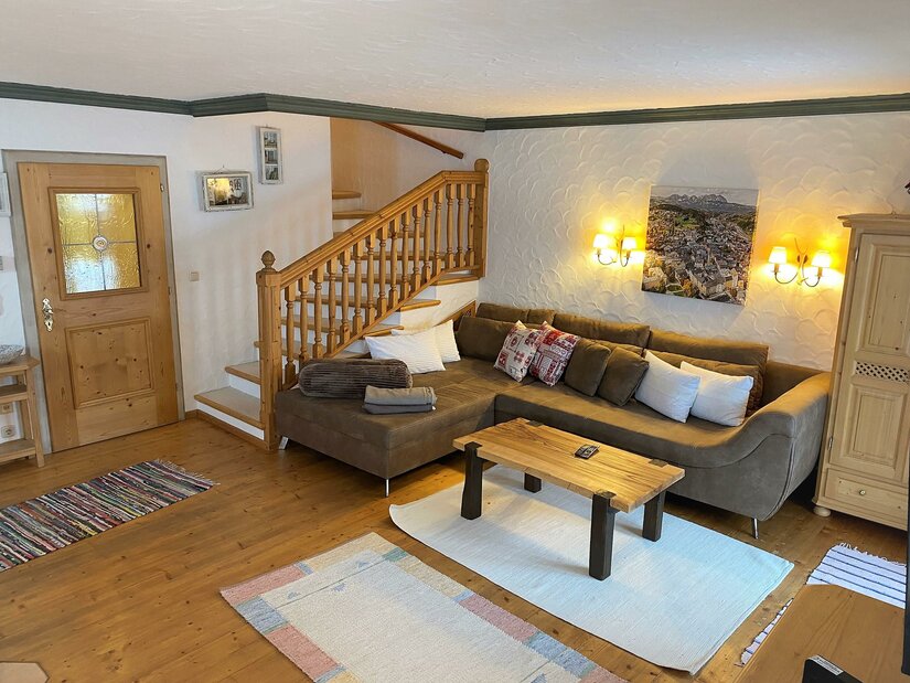 Wohnbereich Haus Staudach Rustikaler Wohnbereich mit braunem Ecksofa, Holztisch und einer Holztreppe in einem Ferienhaus.