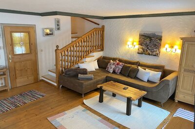 Rustikaler Wohnbereich mit braunem Ecksofa, Holztisch und einer Holztreppe in einem Ferienhaus.