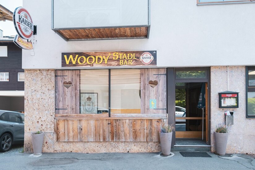Außenansicht der Woody's Stadl Bar mit Holzverkleidung, Herz-Ausschnitten und Firmenschild.