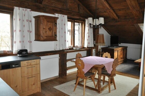 Appartement 1 - Essbereich Rustikaler Essbereich mit Holztisch, Stühlen und Küchenzeile unter einer Dachschräge aus Holz.