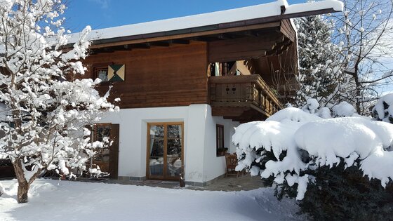 Ferienwohnung Wielemans im Winter Zweistöckiges Holzhaus mit Balkon und schneebedecktem Dach sowie verschneiten Bäumen im Vordergrund.
