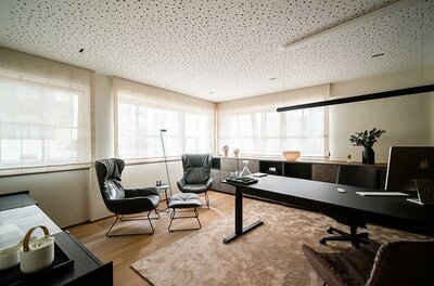 Modernes Büro mit Schreibtisch, zwei Ledersesseln und einer perforierten Decke.