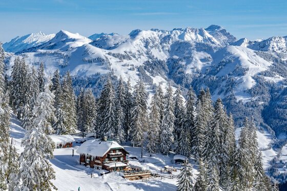 Skigebiet Hahnenkamm im Winter Verschneite Berghütte inmitten von Tannen vor einem alpinen Bergpanorama im Winter.