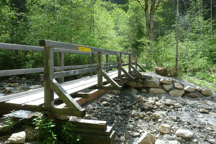 Schleierwasserfall Eine Holzkonstruktion über einen kleinen Bach, umgeben von grünen Bäumen. Der Weg lädt zu einem ruhigen Spaziergang in der Natur ein.