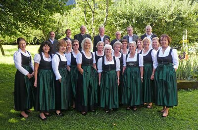 Eine Gruppe von Personen in traditionellen Trachten steht in einer malerischen Landschaft. Sie lächeln und posieren zusammen im Freien.