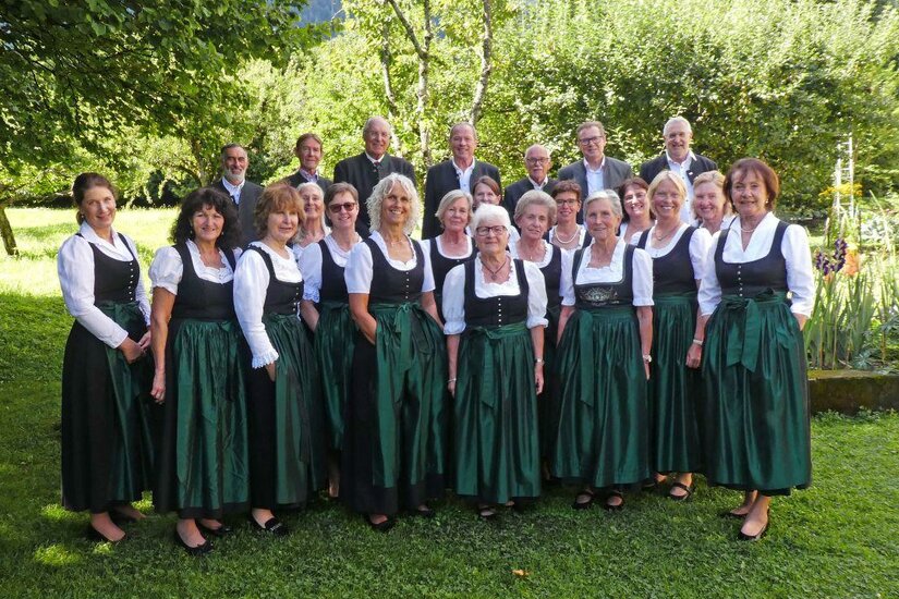 Eine Gruppe von Personen in traditionellen Trachten steht in einer malerischen Landschaft. Sie lächeln und posieren zusammen im Freien.