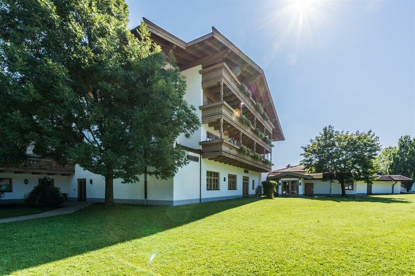 Mehrstöckiges Hotelgebäude mit Holzbalkonen vor einer grünen Wiese unter blauem Himmel.
