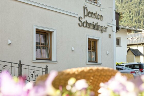 Fassade der Pension Schmidinger Außenansicht der Pension Schmidinger mit Schriftzug an der hellen Hauswand und Fenstern.