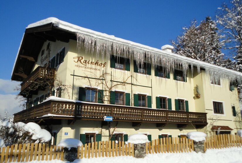 Frühstückspension Rainhof im Winter Gelbes Pensionsgebäude mit schneebedecktem Dach und langen Eiszapfen an der Dachrinne.