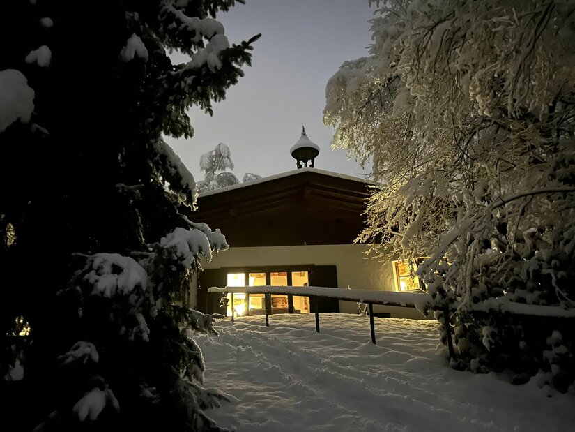 Lutzenberg 19 im Winter Beleuchtetes Gebäude im Schnee bei Dämmerung mit verschneiten Tannen im Vordergrund.