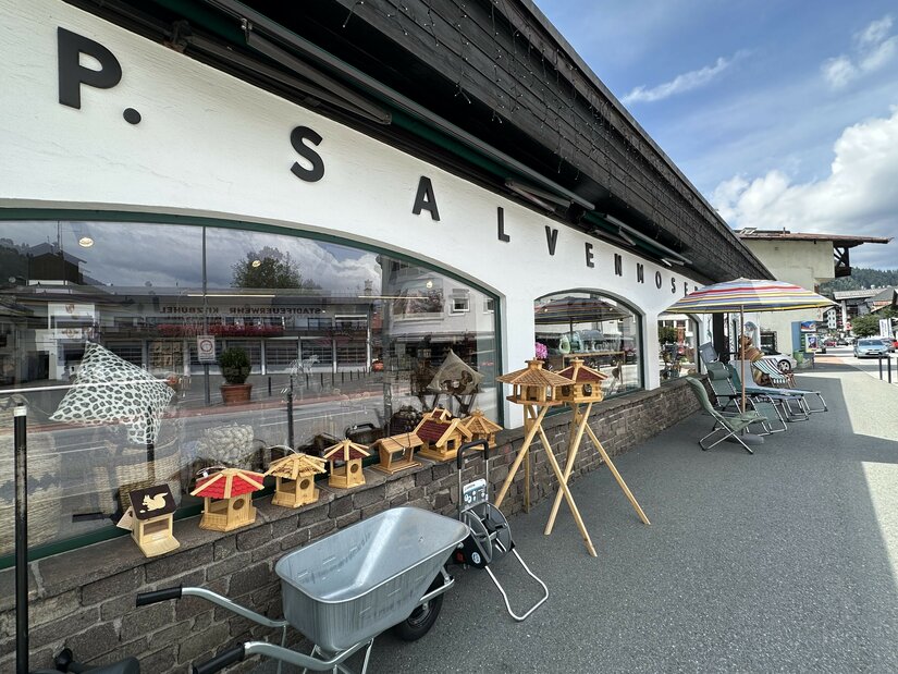 Fachgeschäft Salvenmoser Außenansicht Außenansicht des Geschäfts Salvenmoser mit Vogelhäusern, Schubkarre und Gartenmöbeln vor dem Schaufenster.