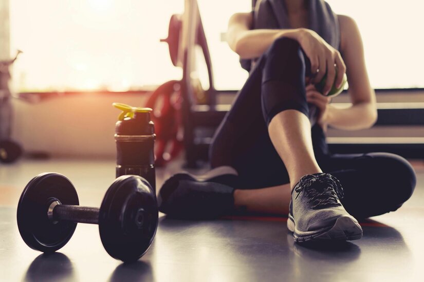 Fitness4Fun im INVIBE Gym Eine Person sitzt in Sportkleidung auf dem Boden eines Fitnessstudios neben einer Hantel und einer Trinkflasche.