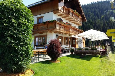 Hollenauer Kreuz Sommer Alpines Gasthaus mit Holzfassade, Balkonen und einer Außenterrasse mit Sonnenschirmen vor bewaldetem Berg.